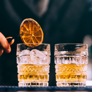 Bartender making a drink with ice and dry orange on a square image